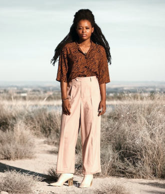 mulher negra com cabelos pretos ventindo uma calça bege